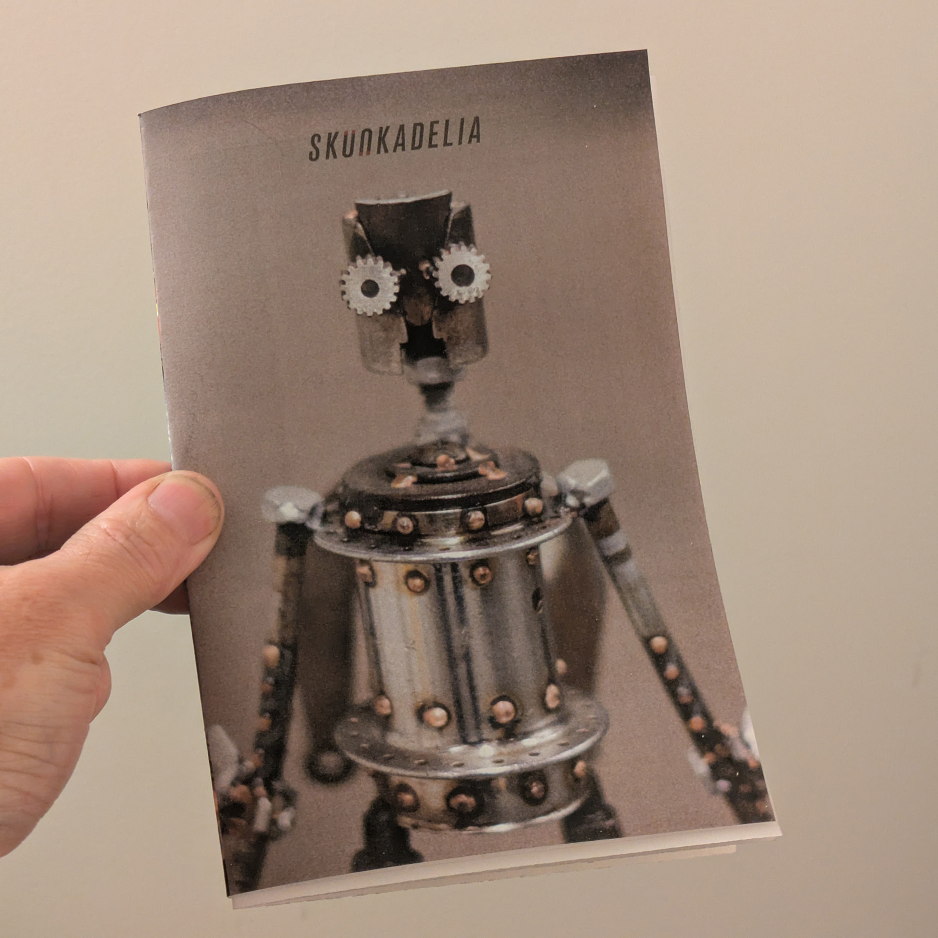 small brochure in hand with a stern looking metal robot figurine on the cover
