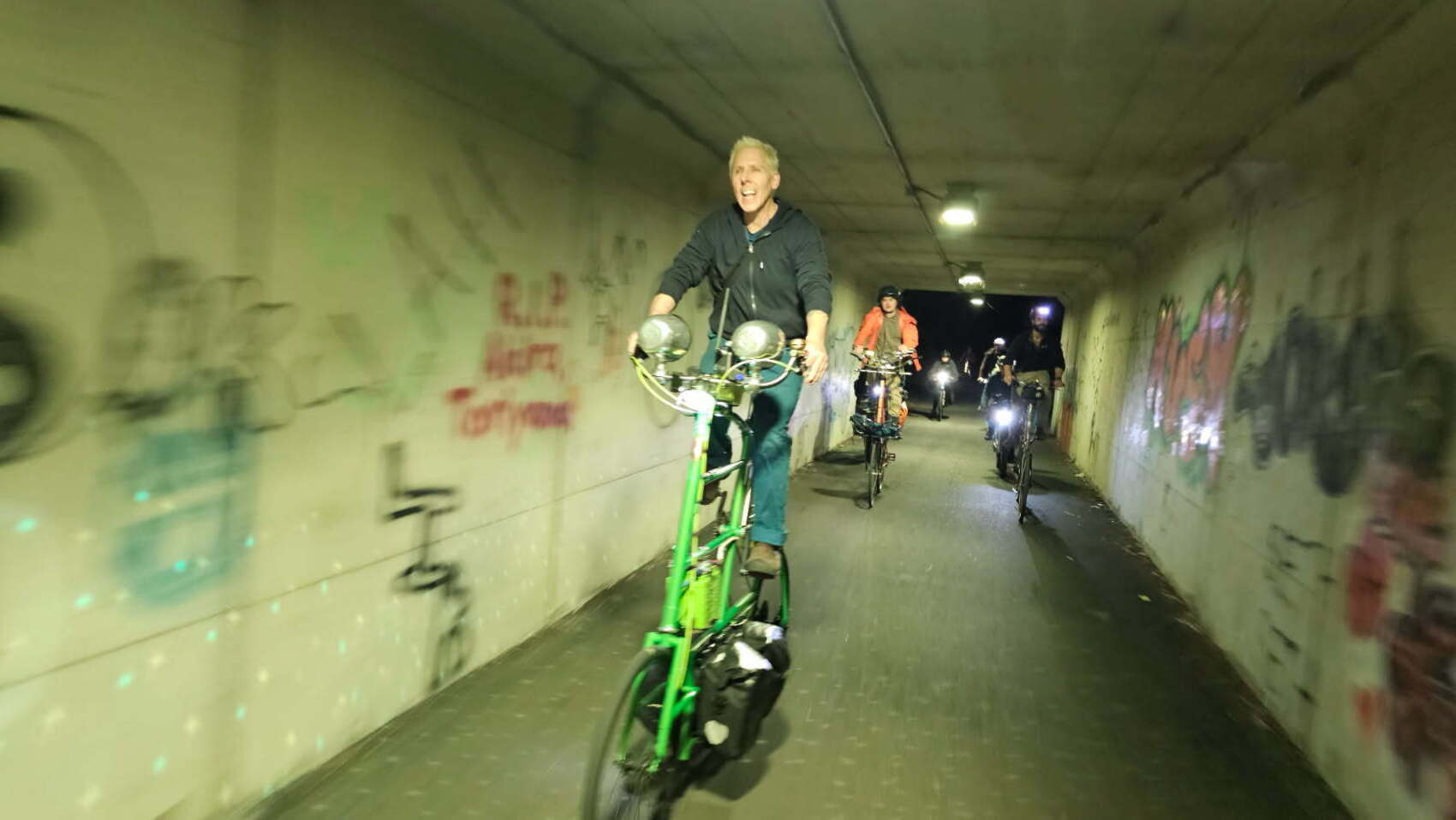 green tallbike lit up and riding fast through a tunnel